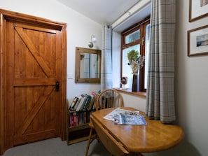 A room with a wooden door, a bookshelf, a table with a magazine, a window with curtains, and a mirror on the wall. - Riverhouse Lodge (Weymouth)