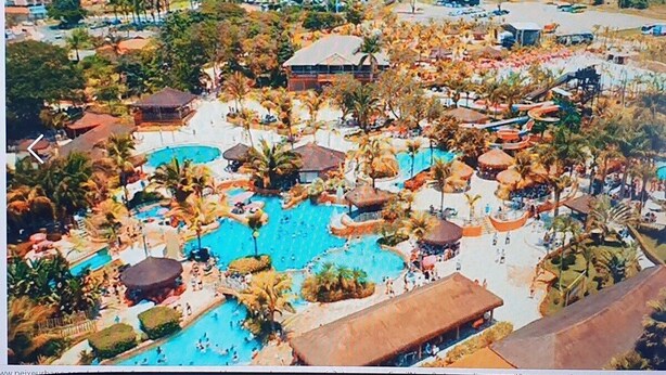 Un complexe hôtelier doté de plusieurs piscines, de palmiers et d’un grand bâtiment en arrière-plan.