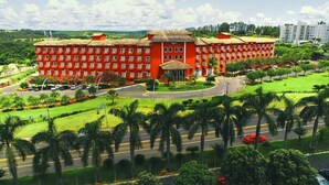 Un grand bâtiment rouge, doté de nombreuses fenêtres, entouré d’une pelouse bien entretenue et de palmiers.