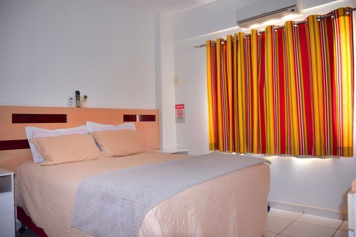 A hotel room with a bed, a nightstand, a wall-mounted air conditioner, and a striped curtain.