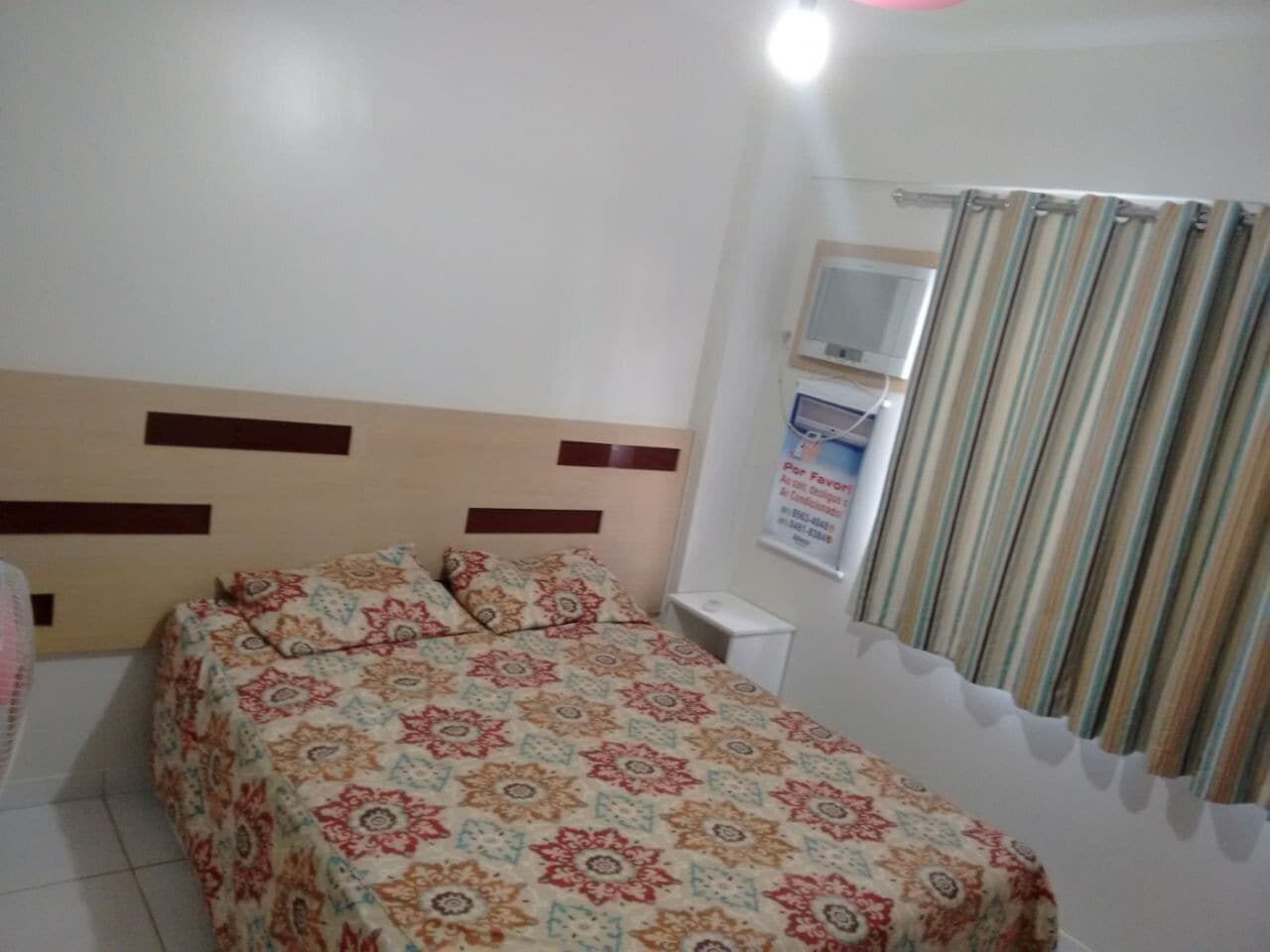 Une chambre à coucher avec un lit, une table de chevet, un miroir et une fenêtre avec des rideaux.