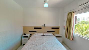 Un dormitorio con cama, mesitas de noche, ventilador de techo, ventana con cortinas y vista a zonas verdes.