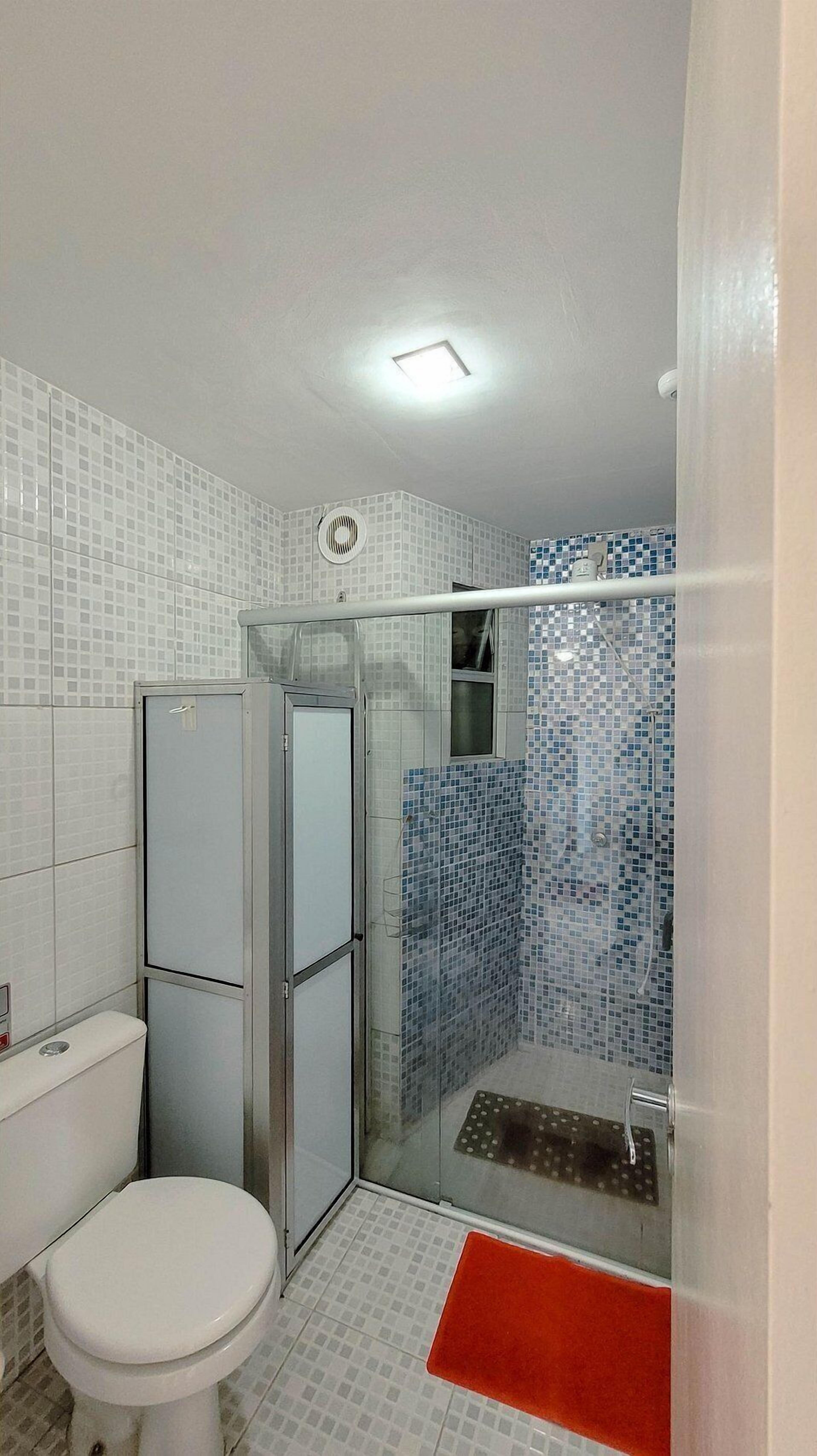 Une salle de bain comprenant des toilettes, un espace douche et des murs carrelés.