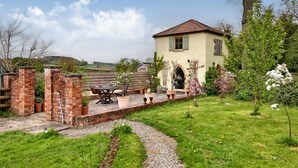 A house with a brick patio, outdoor furniture, and a garden with flowering plants. - The Folly (Hereford)