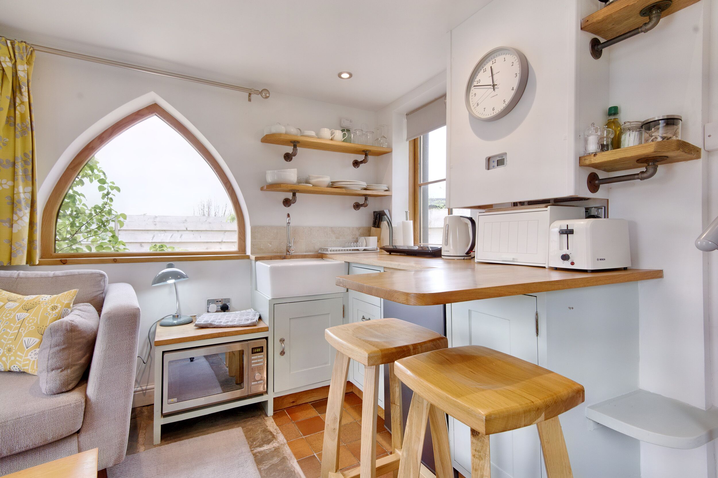 A modern kitchen with wooden shelves, a microwave, a toaster, and a large window.