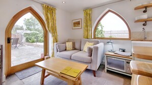 A cozy living room with a sofa, a table, a microwave, and large windows with curtains. - The Folly (Hereford)