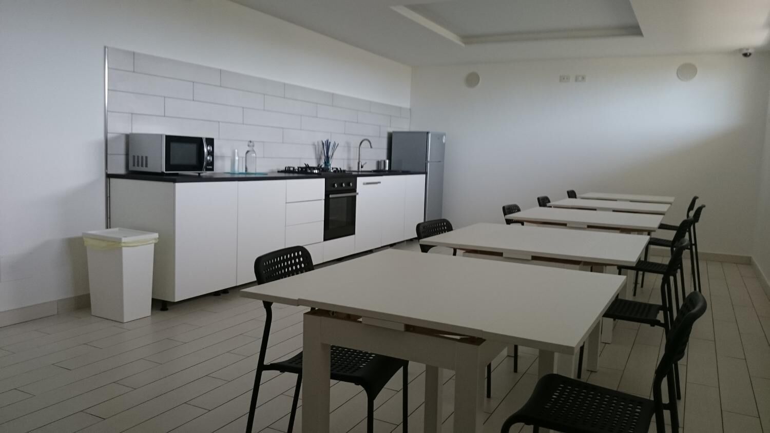 A modern kitchen with white cabinets, a microwave, and a stove. There are six black chairs around a white table.