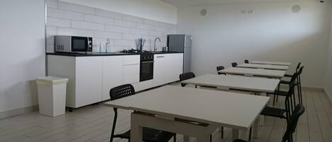 A modern kitchen with white cabinets, a microwave, and a stove. There are six black chairs around a white table.