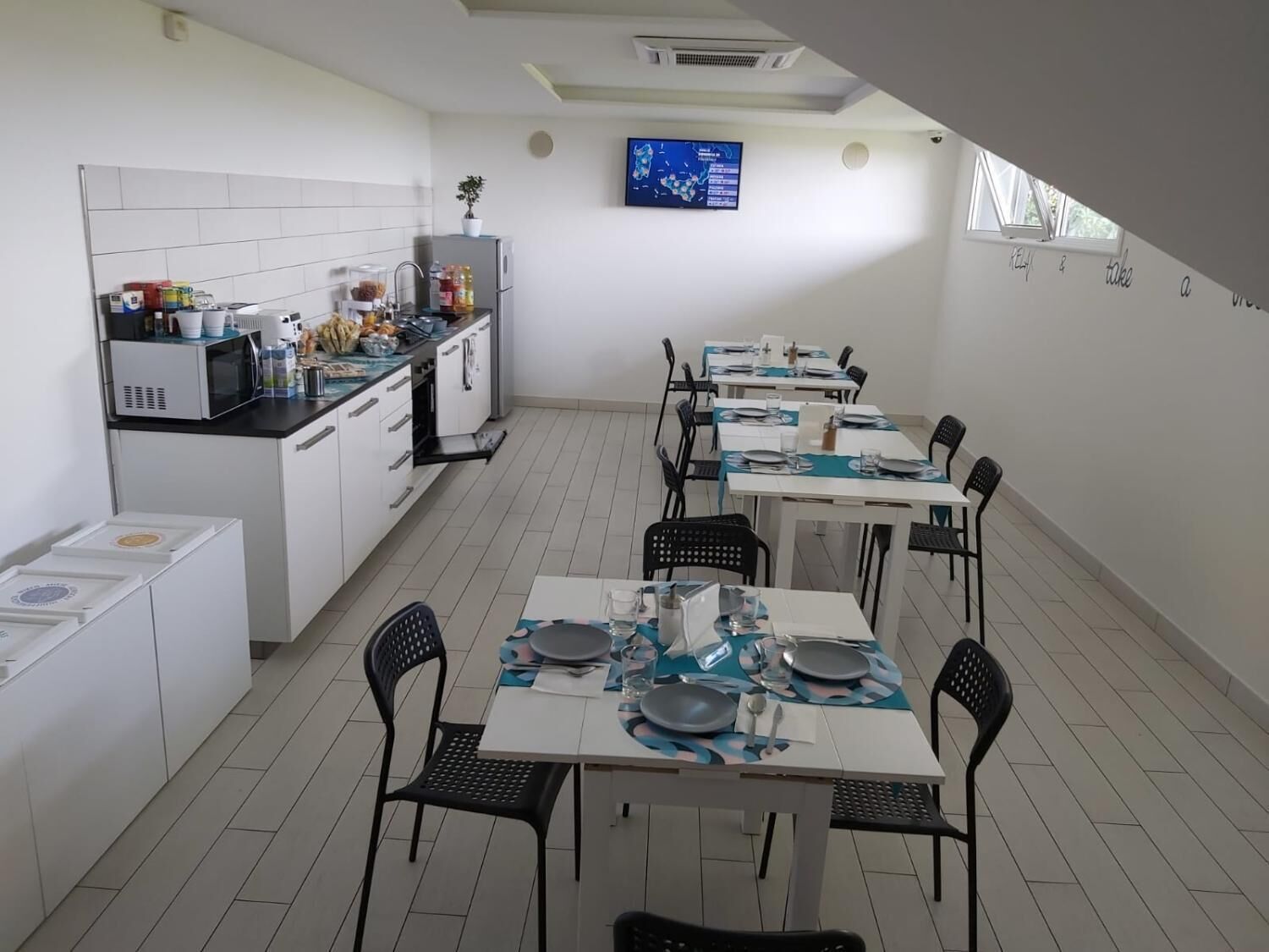 Una cocina moderna con armarios blancos y un comedor con mesas dispuestas para cuatro.