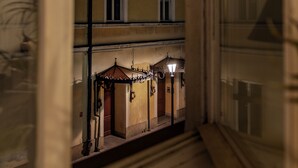 A view through a window of a building with a balcony, a street lamp, and a building with a yellow facade. - 3D FLORIANSKA 15 Apartament (Kraków)