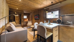 A cozy cabin interior with a wooden ceiling, a dining area with a table and chairs, a sofa, and a kitchen with a sink and cabinets. - Steps from Megève Rink & Chamois Gondolas (Megève)