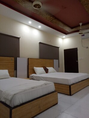A hotel room with two beds, a dark door, and a white ceiling. - pearl cottage (Karachi)