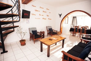Ein modernes Wohnzimmer mit einer Holztreppe, einem Blumentopf, einem Couchtisch und einem an der Wand befestigten Fernseher.