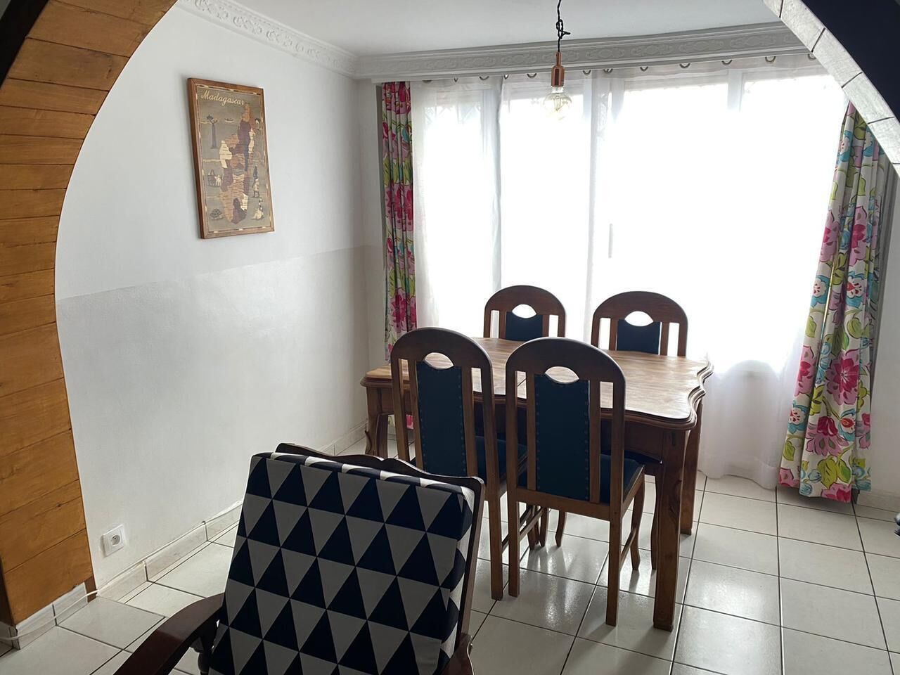 Un comedor con una mesa y sillas de madera, un mapa en la pared y cortinas con estampado floral.