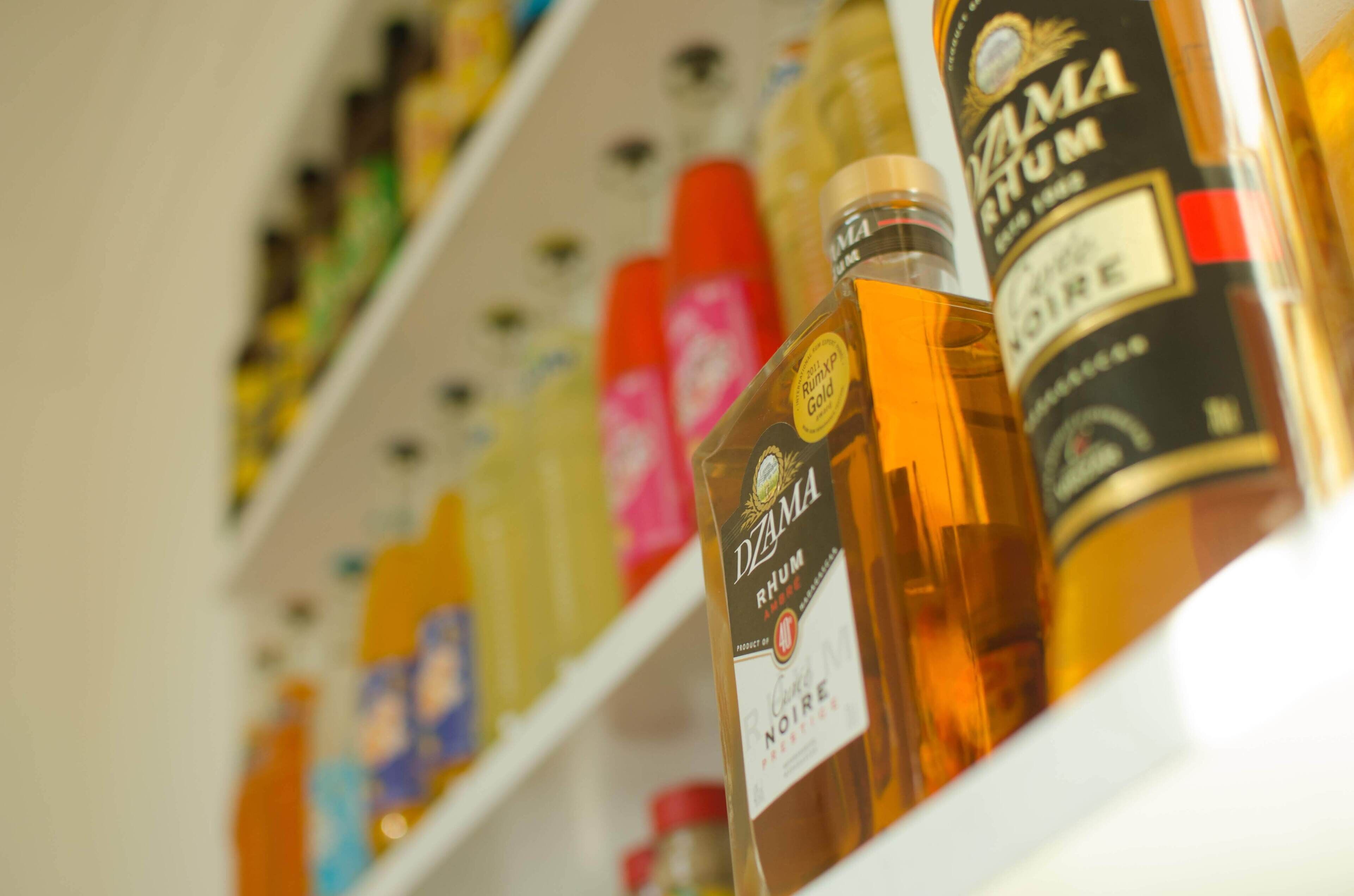Uma prateleira com diversas garrafas de bebidas alcoólicas, incluindo uma garrafa em destaque com a inscrição 'Dzama Rum'.