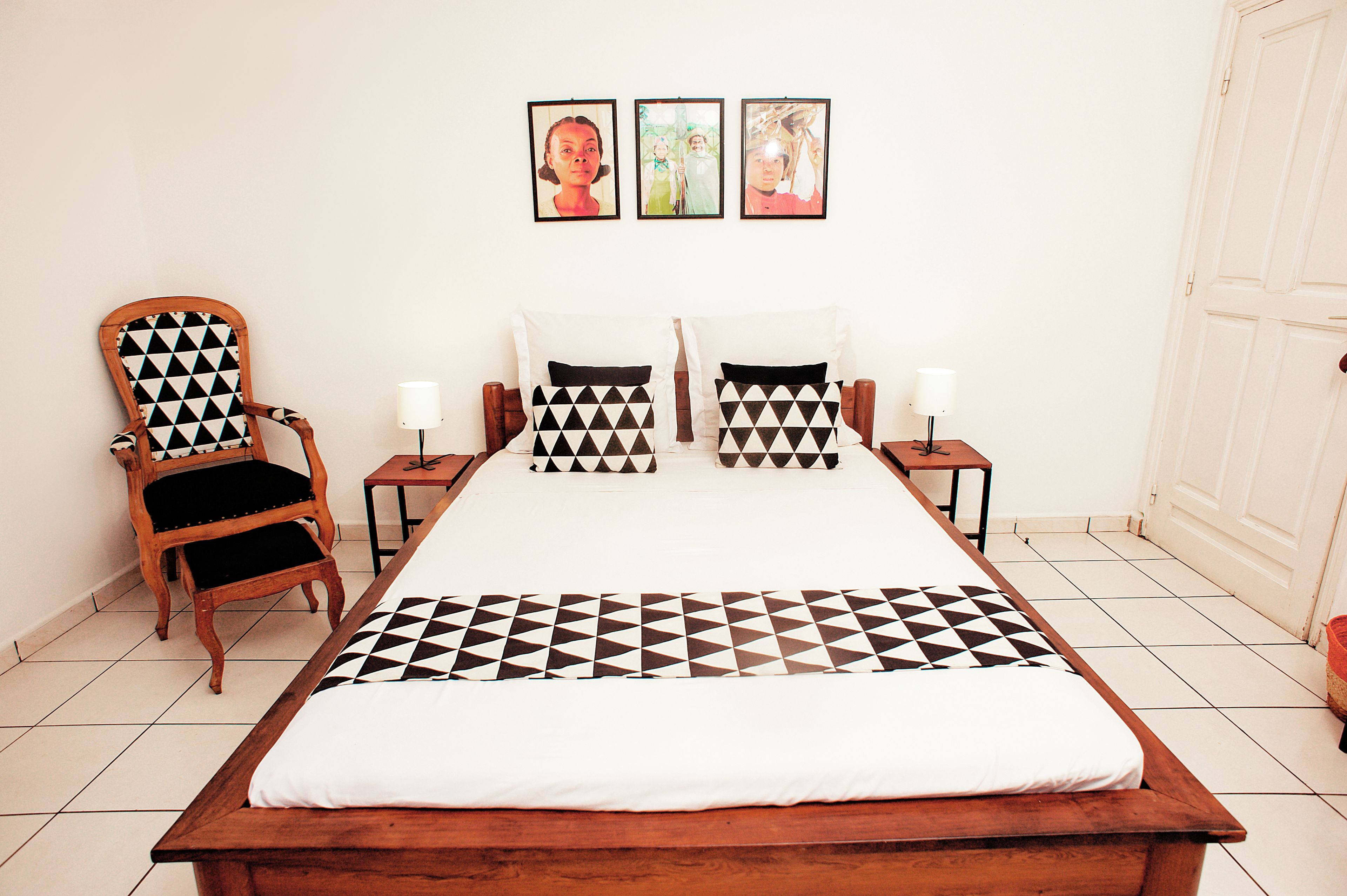 A bedroom with a large bed, two nightstands, a wooden chair, and three framed pictures on the wall.