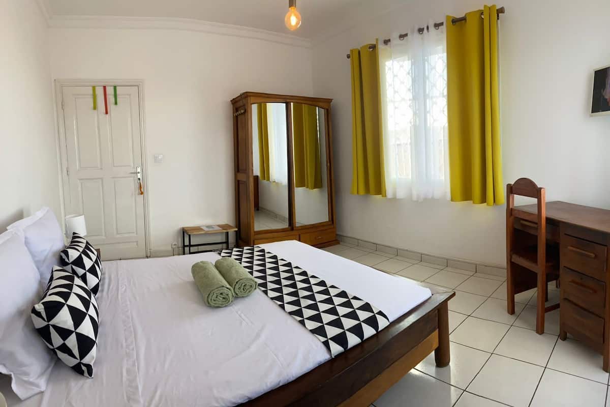 A bedroom with a bed, a wooden desk, a chair, a mirror, and a door.
