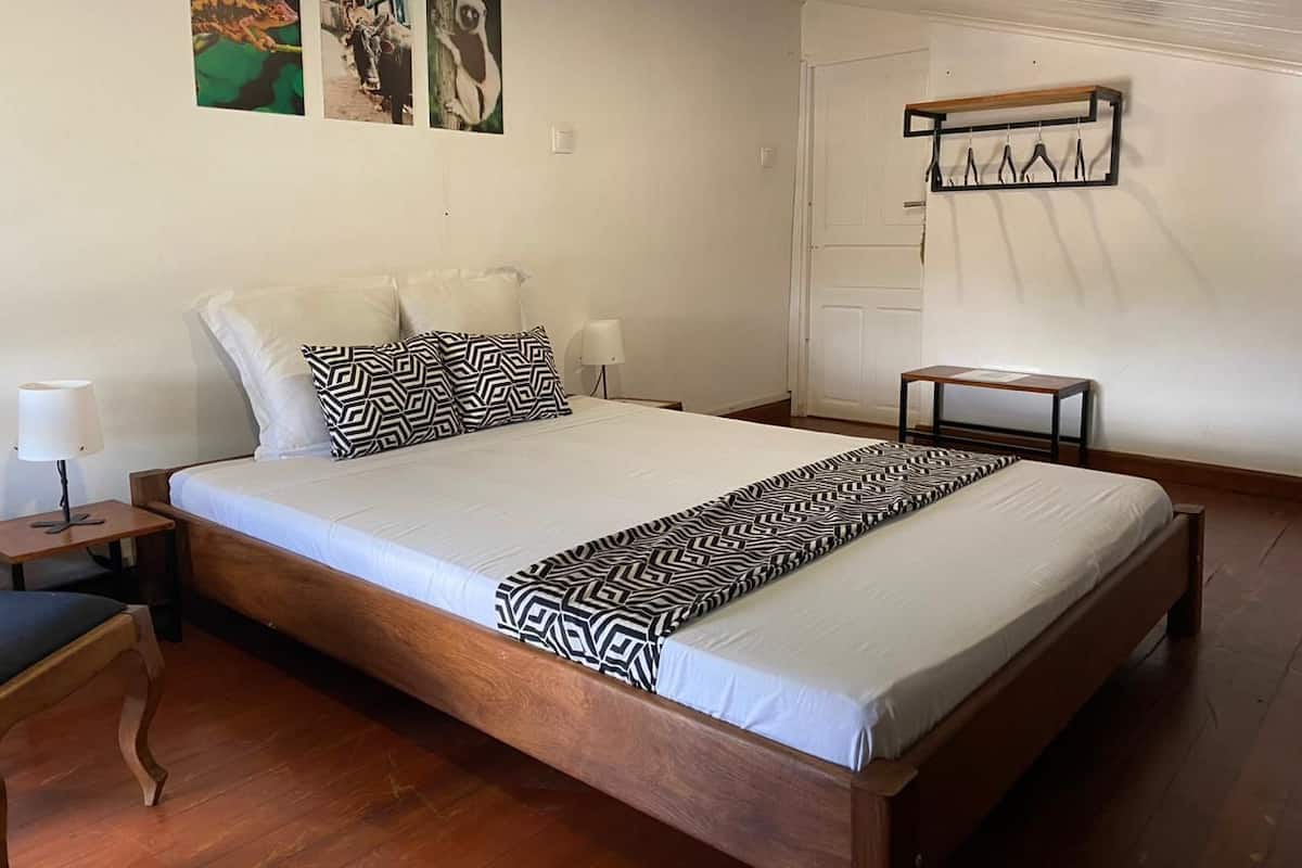 A neatly made bed with a patterned bedspread, a bedside table with a lamp, and a wall-mounted coat rack.