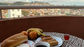 Ein Tisch mit einer Kaffeetasse, einem Gebäckteller und einer Banane auf einem Balkon mit Blick auf eine Stadtlandschaft.