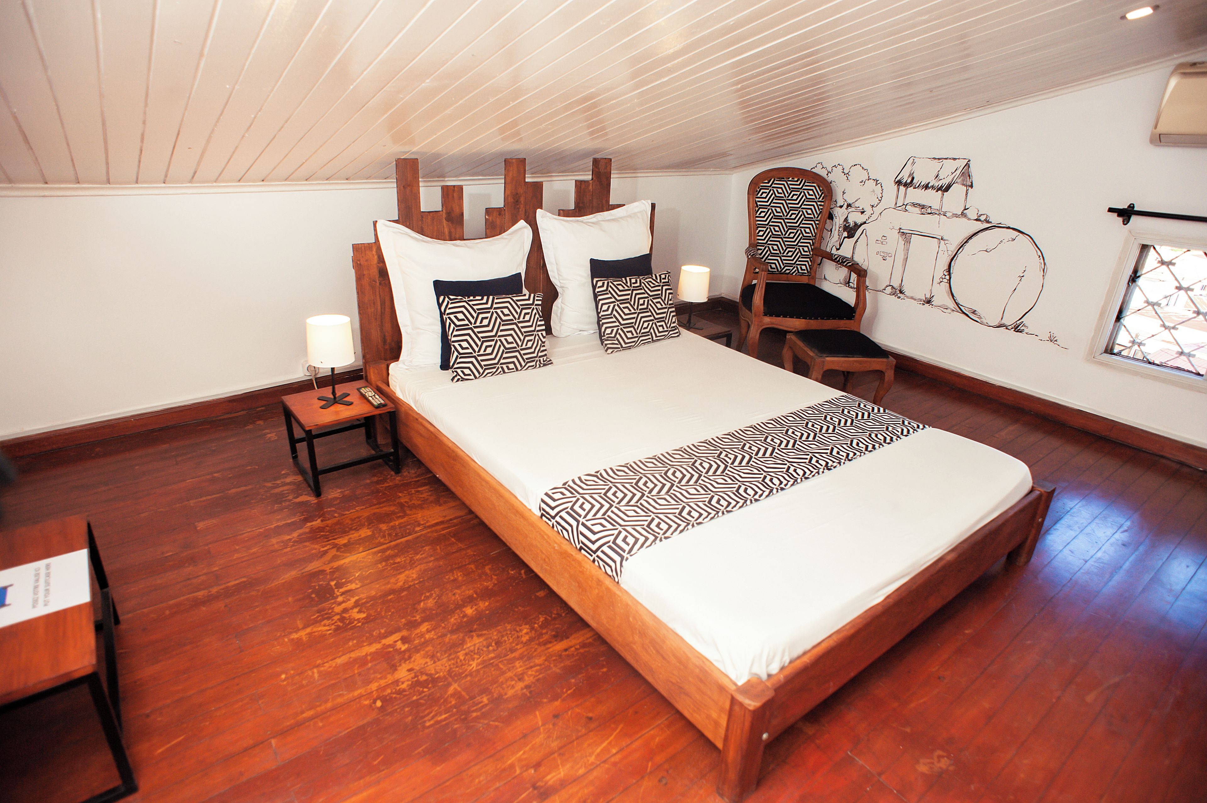 Ein geräumiges Schlafzimmer mit einem großen Bett, einem hölzernen Kopfteil, einem Nachttisch, einem Sessel und einer Wand mit Wandgemälde.