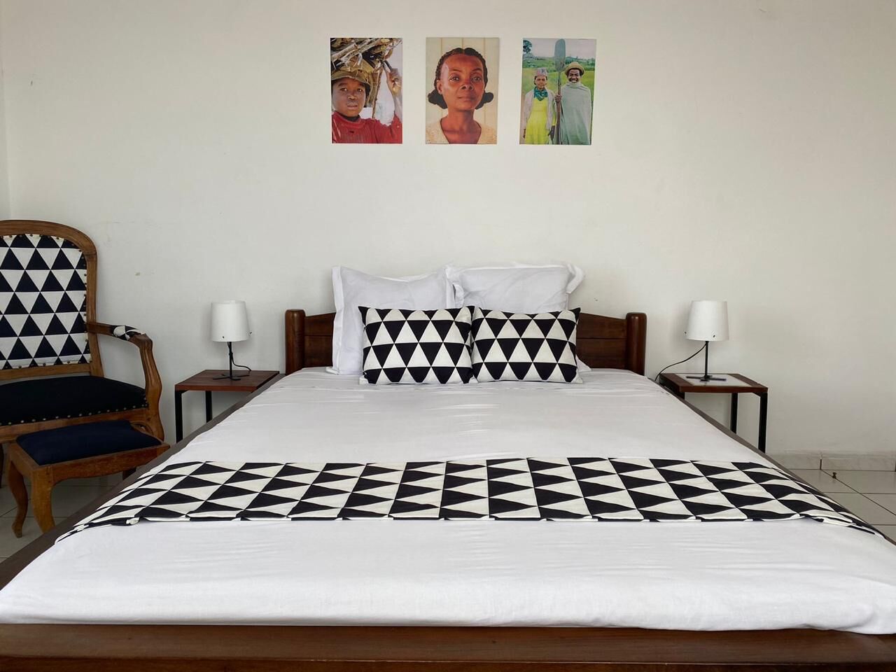 A hotel room with a bed, two bedside tables, a chair, and three wall-mounted paintings.