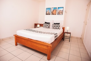 A neatly made bed with a patterned bedspread, a wooden headboard, and two bedside tables with lamps. -  Villa Espoir - Guest house, terrace overlooking Tana, breakfast included (Antananarivo)