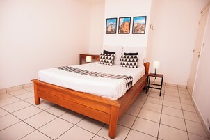 Cama bem arrumada com colcha estampada, cabeceira de madeira e duas mesas de cabeceira com abajures.