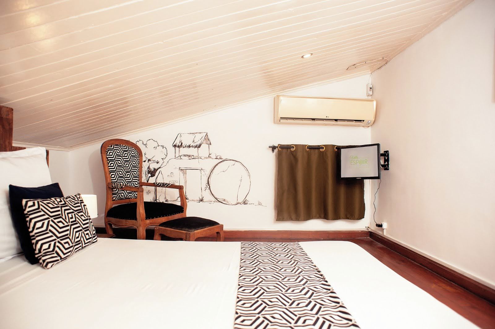 A bedroom with a bed, a chair, a wall-mounted air conditioner, a TV, and a window with curtains.