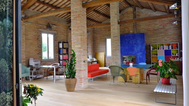 A spacious room with exposed brick walls, wooden beams, a large blue painting, and a variety of seating and tables. - InVento bnb (Civitanova Marche)