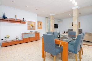 Una sala de estar moderna con una mesa de comedor de vidrio, sillas azules, un aparador de madera y un sofá.