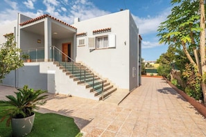 Una casa moderna de dos pisos con una escalera que lleva al piso superior, un porche cubierto y un camino de entrada pavimentado.