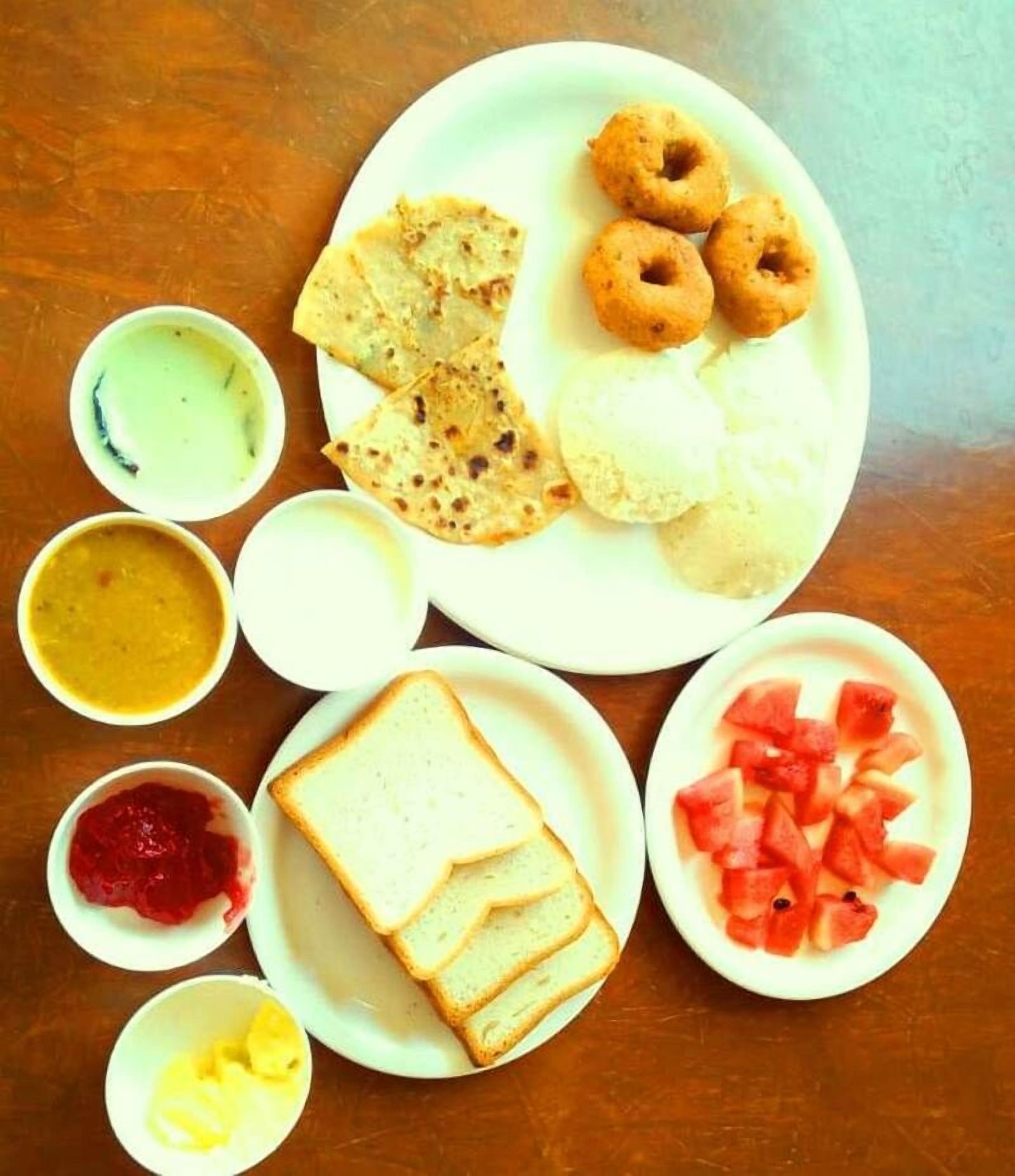 Une table est dressée avec divers aliments, notamment des galettes, une assiette de tranches de pain, une assiette de tranches de pastèque et plusieurs petits bols contenant différentes sauces et condiments.