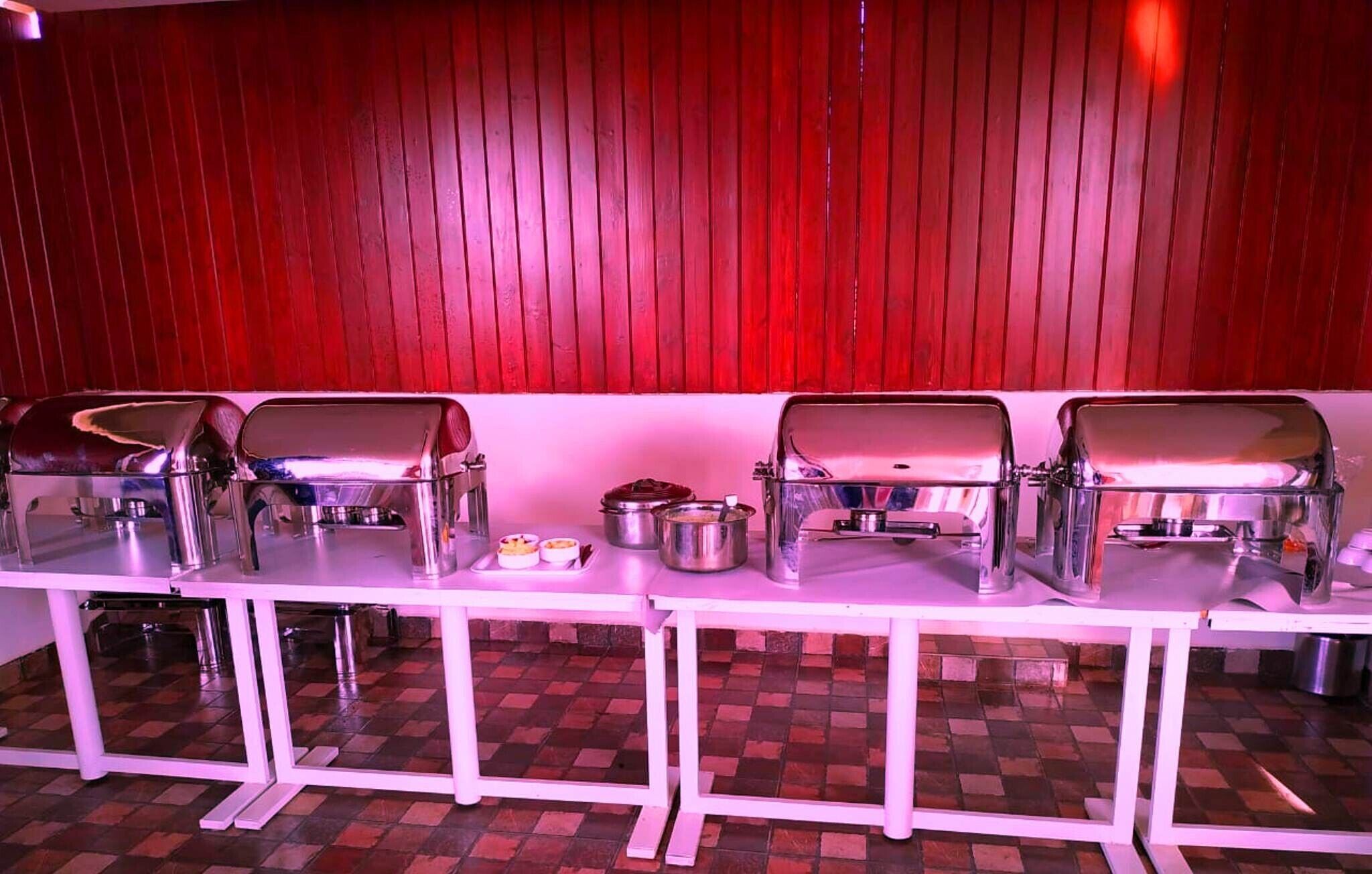 A buffet setup with multiple stainless steel chafing dishes on a white table against a red wall.