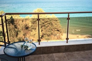 A round table with two wine glasses and a flower on a balcony overlooking a beach and forest.