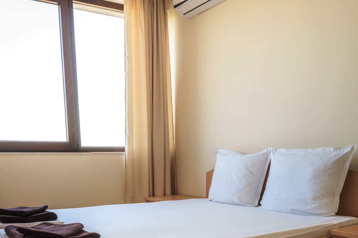 Ein Hotelzimmer mit Bett, Fenster mit Vorhängen, Klimaanlage und Nachttisch.