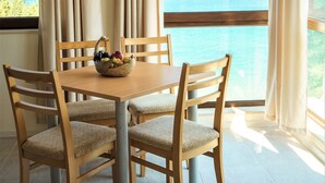 A dining area with a table and four chairs, a bowl of fruit, and a view of the ocean through large windows. - Moreto Seaside Aparthotel (Obzor)