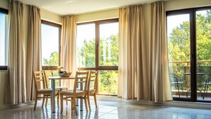 A spacious room with a large window, a dining table with chairs, and a view of greenery outside. - Moreto Seaside Aparthotel (Obzor)