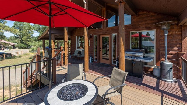 Eine Holzterrasse mit Sitzgelegenheiten im Freien, einem Grill und einem roten Sonnenschirm.