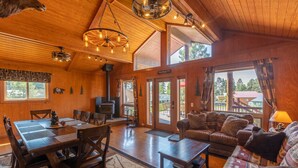 Ein gemütliches Chalet-Interieur mit Essbereich, Kamin, Sofa und großen Fenstern mit Blick ins Freie.