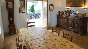 A dining area with a table set for four, a wooden cabinet with decorative items, a wall clock, and a painting. - La Maison Blanche: private heated pool, 7 bedrooms (Sarlat-la-Canéda)
