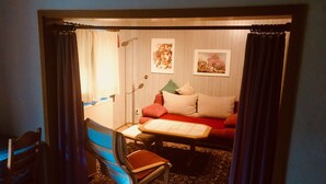 Ein kleines Zimmer mit Bett, Stuhl, Schreibtisch und Stehlampe.