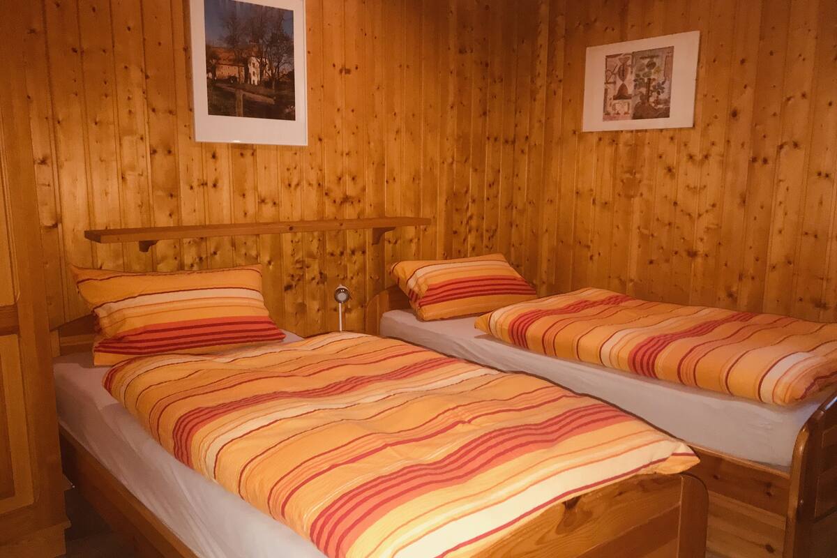 Quarto de madeira com duas camas, cada uma com roupa de cama listrada.