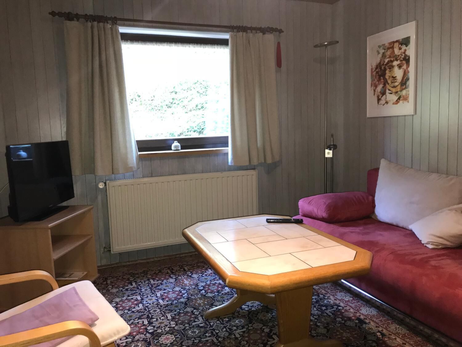 A room with a wooden table, a red sofa, a television, and a window with curtains.