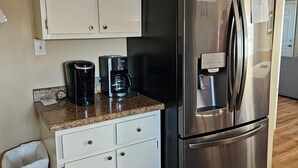 Een compacte keuken met witte kastjes, een roestvrijstalen koelkast en een koffiezetapparaat op het aanrecht.
