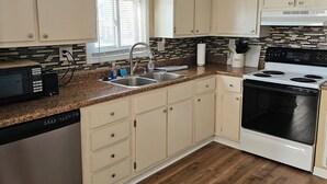 Een keuken met beigekleurde kastjes, een witte oven, een vaatwasser en een raam met zonwering.