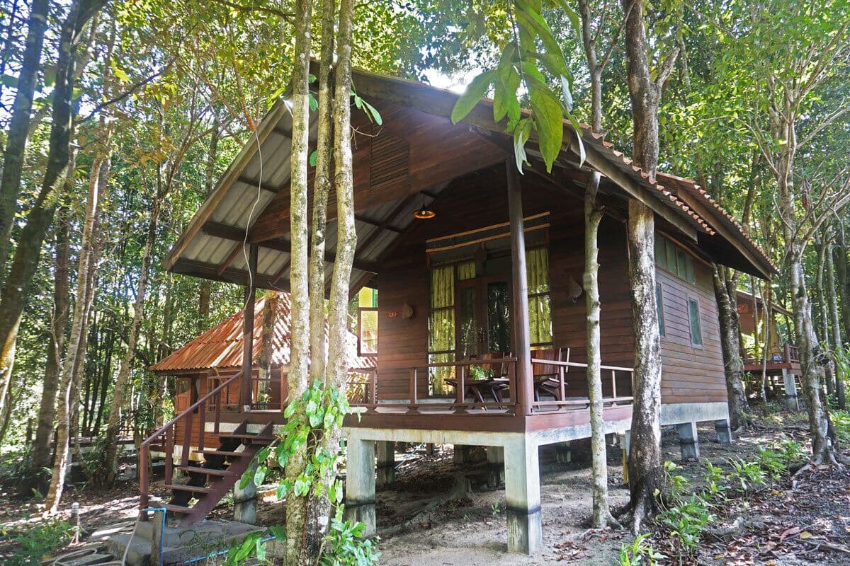 A wooden cabin with a porch and staircase, surrounded by trees.