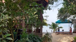 A beachside area with a wooden structure, a covered seating area, and lush greenery. - Baan Klong Kleng (Ranong)