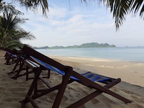 A beach with wooden lounge chairs and a palm tree. - Baan Klong Kleng (Ranong)