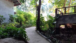 A concrete pathway flanked by large rocks and potted plants, leading to a rustic building with a wooden bridge overhead. - Baan Klong Kleng (Ranong)