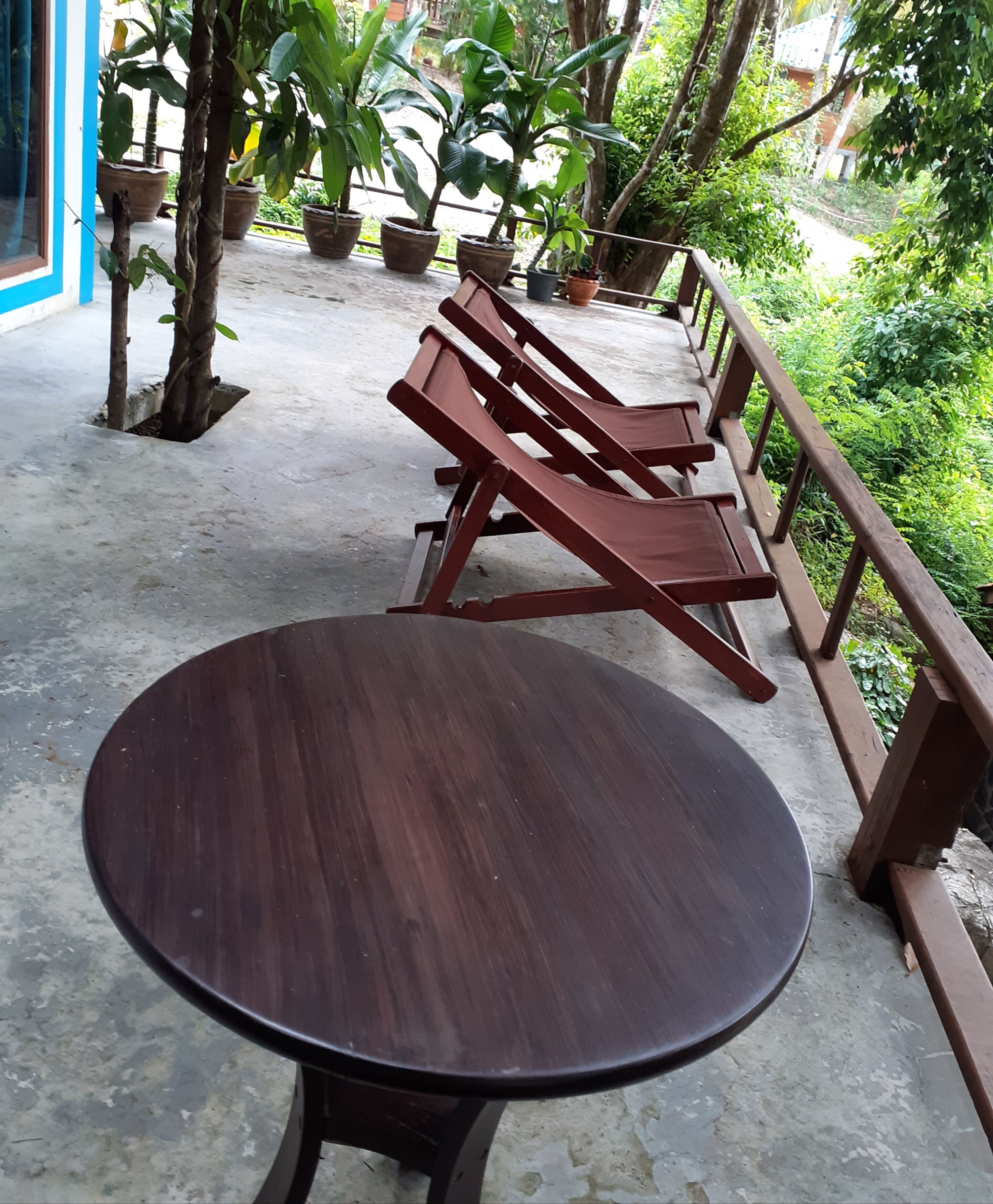 Een ronde houten tafel met metalen frame, omgeven door een betonnen vloer en een houten leuning.